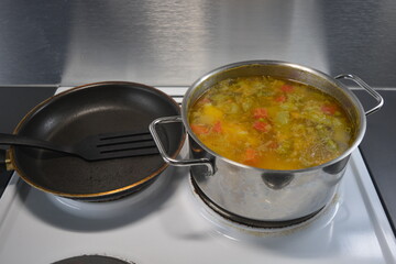 Cooking delicious and healthy food, hot fresh soup from vegetables and meat. The hot dish is cooked in a metal pot and placed on a white kitchen stove.