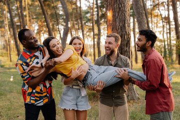 Multiracial group of people, friends throwing a girl in the air and having fun