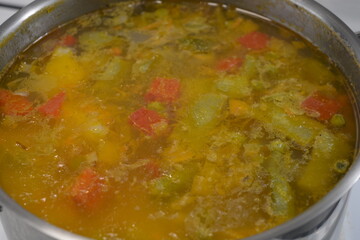 Cooking delicious and healthy food, hot fresh soup from vegetables and meat. The hot dish is cooked in a metal pot and placed on a white kitchen stove.