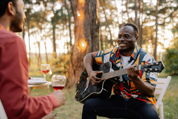 African man plays the guitar for Indian man who drinks wine and sings