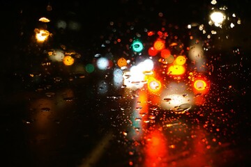 Abstraktes Motiv mit Auto auf nasser Straße und bunten Lichtern in Stadt vor schwarzem Himmel bei Sturm, Regen und Kälte im Winter