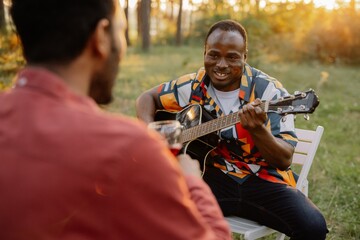 African man plays the guitar for Indian man who drinks wine and sings