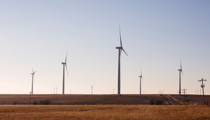 Wind turbines in a field in Kansas.  Side view. Utility lines and rural  road visible.