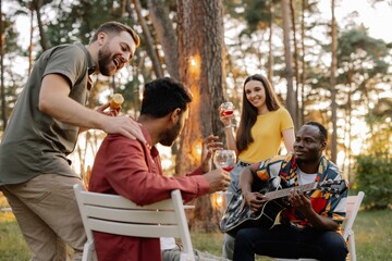 Multiracial group of friends, African man playing guitar around happy friends drinking wine