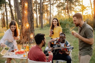 Multiracial group of friends, African man playing guitar around happy friends drinking wine