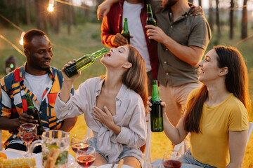 Funny pretty woman quickly drinking beer with cheerful multiracial friends at dinner party