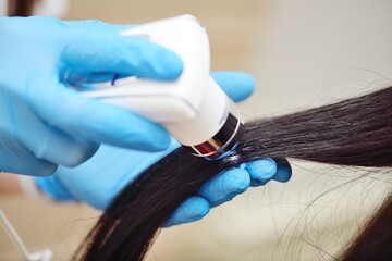 doctor cosmetologist dermatologist diagnoses the condition of the patient's hair using a special...