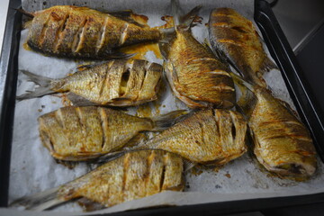 Delicious and healthy, baked fish, Carassius with lemon on a black baking sheet with white parchment paper.