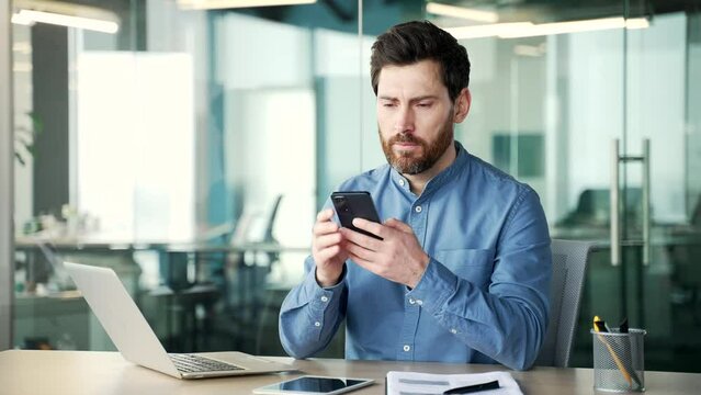 Worried manager having problems with software or service on smartphone mobile phone sitting at workplace in business office. Frustrated disappointed worker complains about bad internet connection