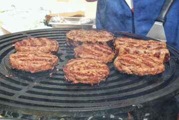 Grilled hamburger meat at barbecue in home backyard. Burgers cooking on gas grill with smoke outdoor. Process of preparing cutlet on grill with burning coals. Street food eat cafe on open fire