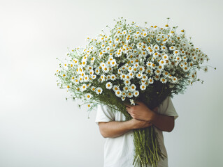 Man in white t-shirt hiding behind a large bouquet of wild daisy flowers, on white background. Flowers from the garden for birthday, anniversary, midsummer celebration. Copy space.
