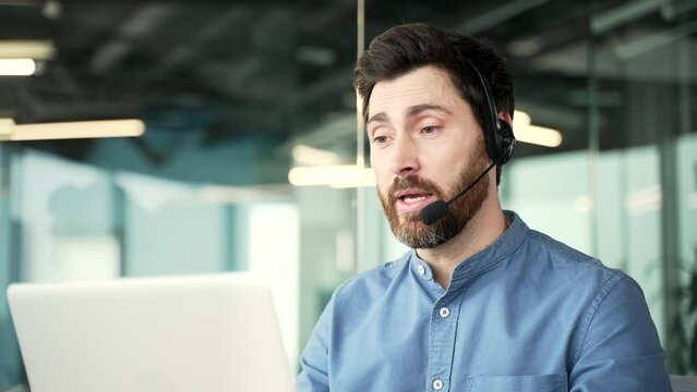 Confident operator who works in customer support speaks on a video call using a laptop. Call center agent in wireless headset helping customer with complaints in office. Online consultation. Close up