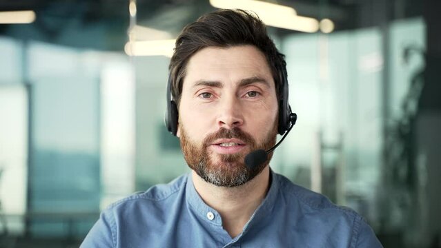 Webcam view. Businessman in headset talking on a video call looking at the camera sitting in office. Entrepreneur has a business meeting. Call center agent helping customers with complaints. Close up
