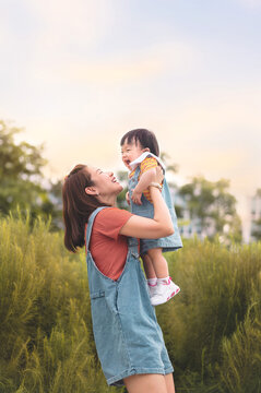Happy Asian mother plays with daughter and holding girl in hands at park with nice sky, Baby smile and laughing,  Family concept.
