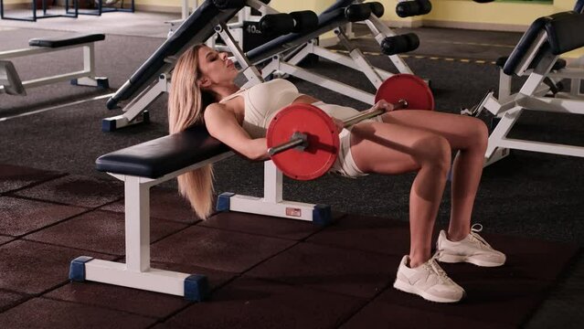 Young woman performing barbell hip thrust in gym.