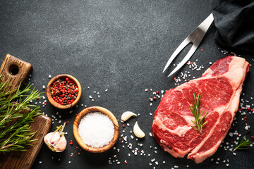 Beef steak with spices on black background. Ribeye steak raw meat. Top view with copy space.