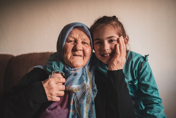 Close up portrait of a happy little girl with her senior Muslim grandmother at home