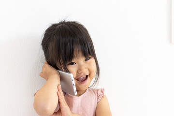 スマートフォンで電話をする笑顔の女の子（3歳、日本人）