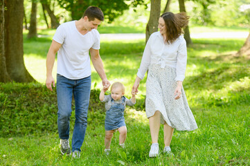 Obraz premium Child walks in the park on the grass holding hands with his parents, learns to walk, take his first steps.Happy family