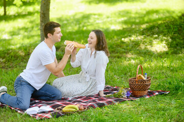 A couple in love, a man and a woman, cheerfully feed each other a baguette in the fresh air during...