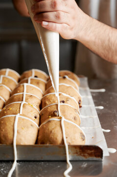 Baker piping 'cross' onto uncooked fruit hot cross buns made with yeast and sourdough