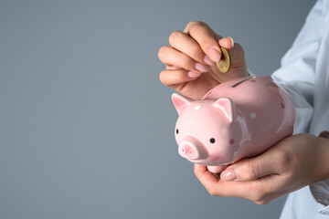 A woman puts a penny in a piggy bank, studio background
