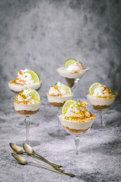 Arrangement of lime parfaits and cookie crumbles in vintage cocktail glasses with lime garnish on gray background