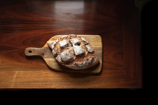 Rustic bread loaf on wooden chopping board on antique wood.