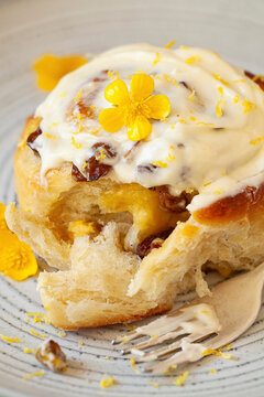A lemon roll filled with lemon curd, sried fruit and pistachio nuts and topped with cream cheese forsting on a plate.