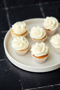 Mini vanilla cupcakes on a white plate and black tile background