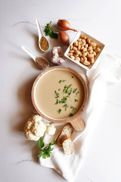 Cauliflower, Cumin and Lima Bean Vegan Soup with Ingredients on White Marble Benchtop. Minimal flatlay.