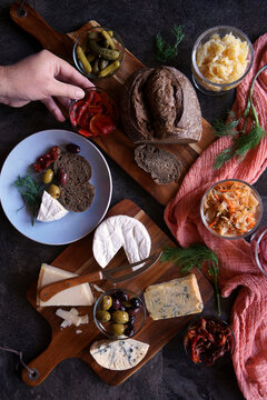 Healthy probiotic cheese platter served with kimchi, dark dye sourdough bread, and fermented vegetables. Male hand reaching for food.