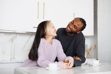 Cheerful young diverse couple holding hands near coffee in modern kitchen at home