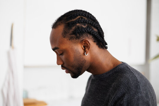 Profile of young african american man with braids hairstyle in sweatshirt in blurred kitchen