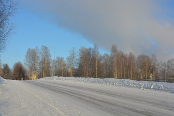 A real snowy Finnish winter in Varkaus, Finland. White snowy road with birches, fir trees, spruces growing in wildlife and illuminated by a lot of sunlight.