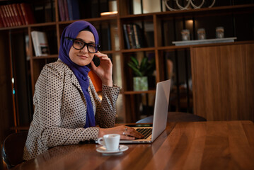 A happy young Muslim business woman in hijab working on a laptop at office