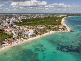 Aerial drone view of beach with blue transparent Caribbean Sea with buildings and large green vegetation area on a beautiful day with cloudy blue sky in Playa del Carmen 