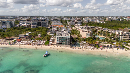 Drone aerial view of coastline in Playa del Carmen with white sand beach with tourists and building on a sunny day with cloudy blue sky