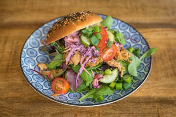 Pulled chicken sandwich with cucumber, tomato, coleslaw and salad on a wooden table