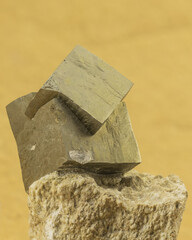 Pyrite crystal formation prominently displayed on natural rock against yellow backdrop