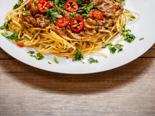 Spaghetti Bolognese dish with pasta, red sauce, minced beef, red peppers and green fresh herbs on white plate and light color table cloth. High quality products in a tasty Italian style dish.