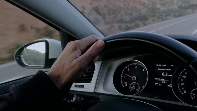 Close-up shot of hand driving a car showing the road
