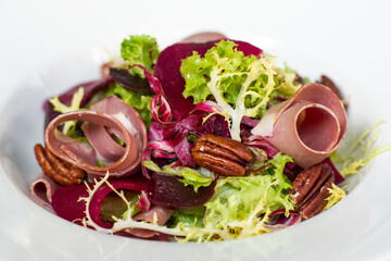 Close up of roast beef and beetroot salad with pecan nuts in white bowl