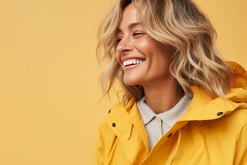 Portrait of smiling woman in yellow raincoat on yellow background.
