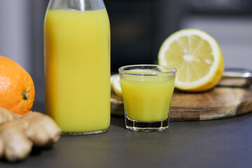 Homemade orange, lemon and ginger drink in a glass bottle with a small shot glass
