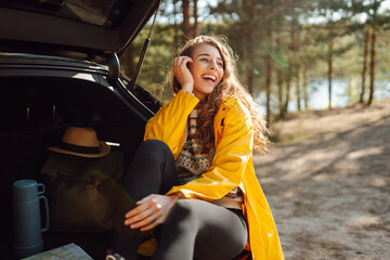 Young woman sits in the trunk of a car in the forest. The concept of traveling by car, active...