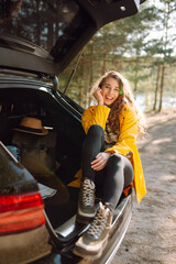 Young woman sits in the trunk of a car in the forest. The concept of traveling by car, active lifestyle.