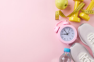 Time to get active: embracing fitness for a healthier you. Top view photo of alarm clock, trendy sneakers, yellow dumbbells, measure tape, apple, water on pastel pink background with promo panel