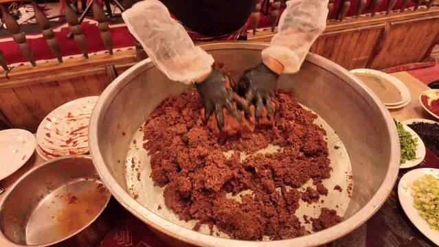 A chef is kneading a cig kofte traditional Turkish raw meatball in a copper tray during traditional Sira Night.