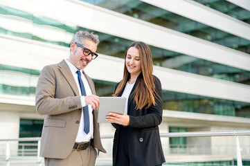 A mature businessman and his colleague review content on a tablet, reflecting on a blend of traditional business acumen and modern technology, indicative of a diverse and tech-savvy corporate world